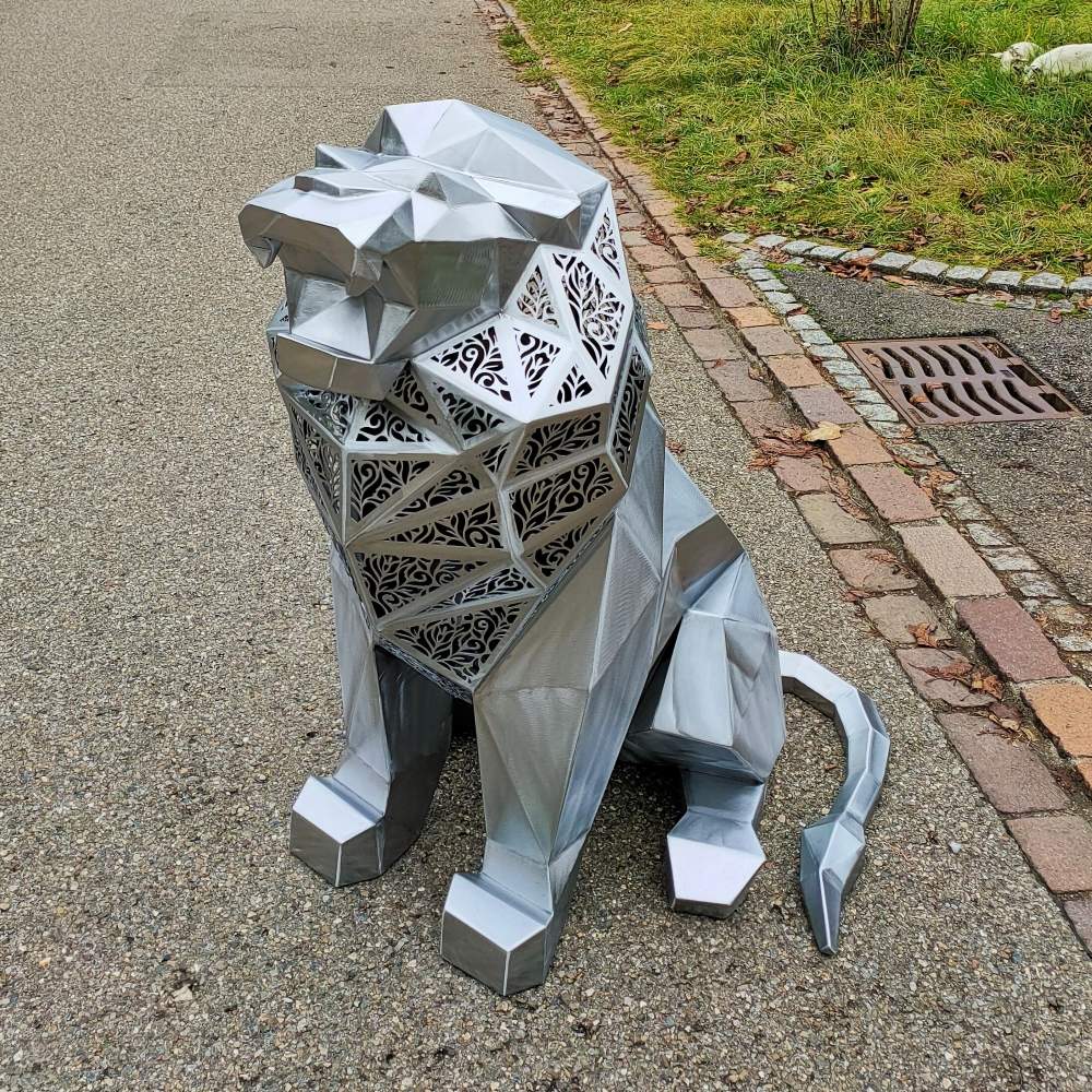 Polished silver geometric lion sculpture with laser-cut panels, posed on a paved path